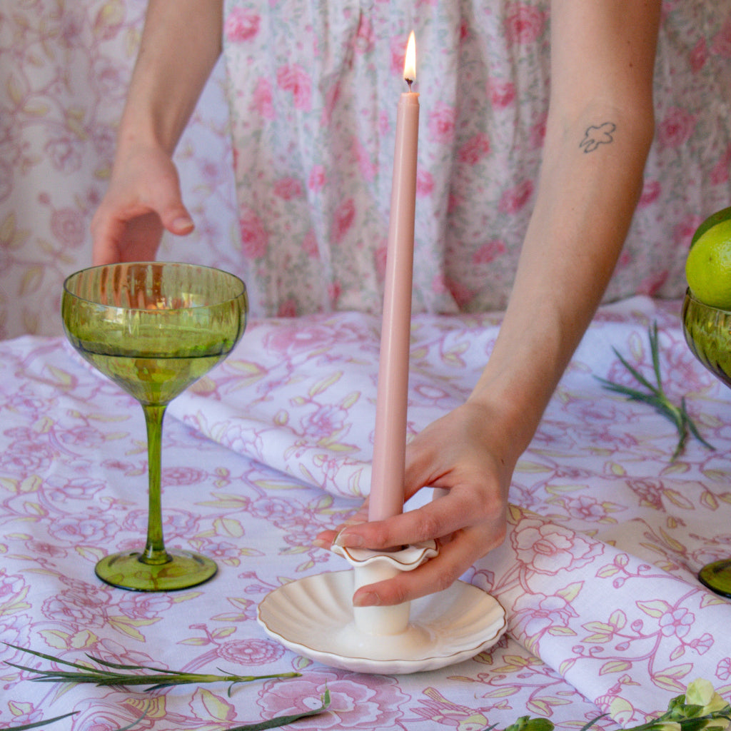 Pink taper candle in a cream ceramic candle holder beside a green coupe on floral table linen
