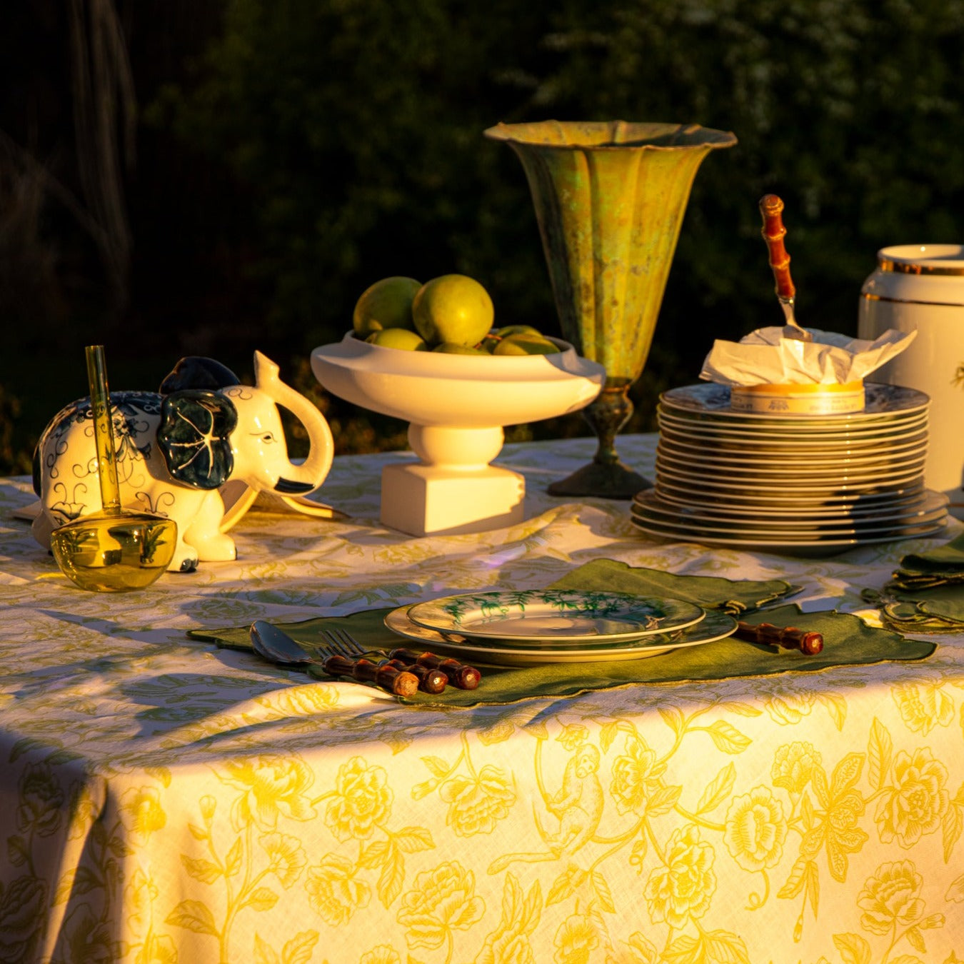 Sun lights up safari table with white linen featuring a delicate pistachio green design of subtle monkeys and floral patterns